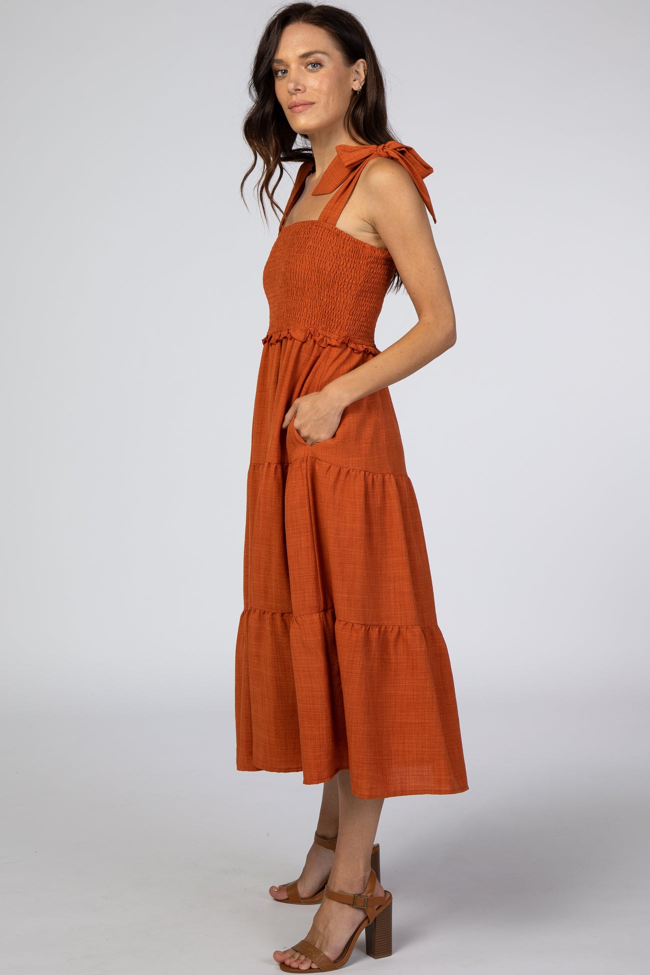 woman wearing an orange smocked midi dress with tie straps and side pockets