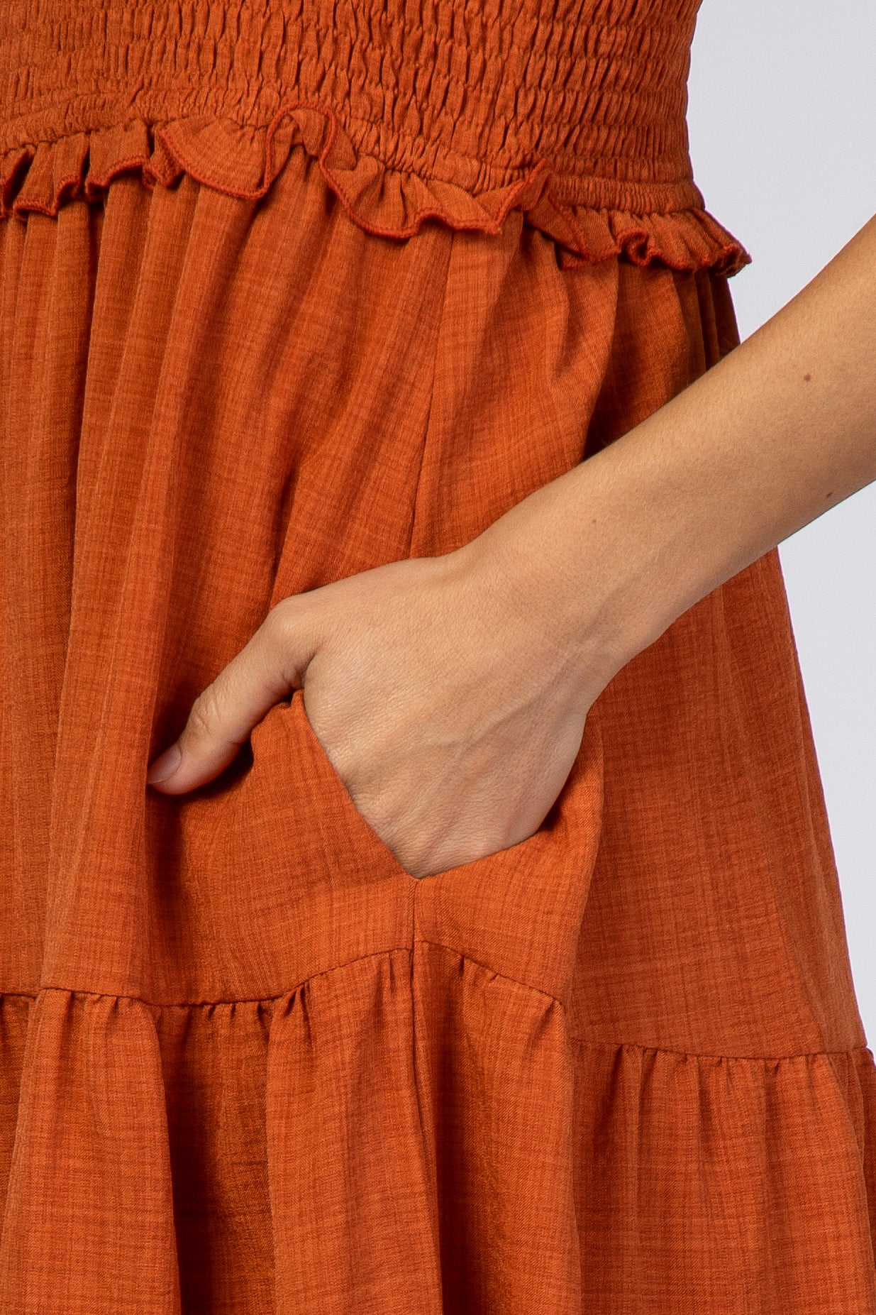 close-up of a woman holding a pocket in an orange smocked tiered dress with ruffle details