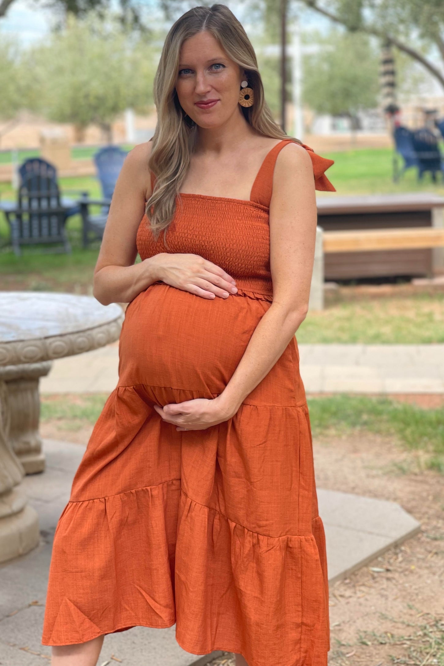 woman wearing an orange maternity dress with smocked bodice and tiered skirt, holding her baby bump