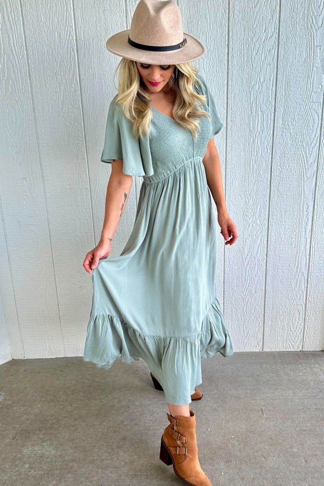 woman wearing a mint green maxi dress with short sleeves and a flared hem, paired with a beige hat and brown ankle boots