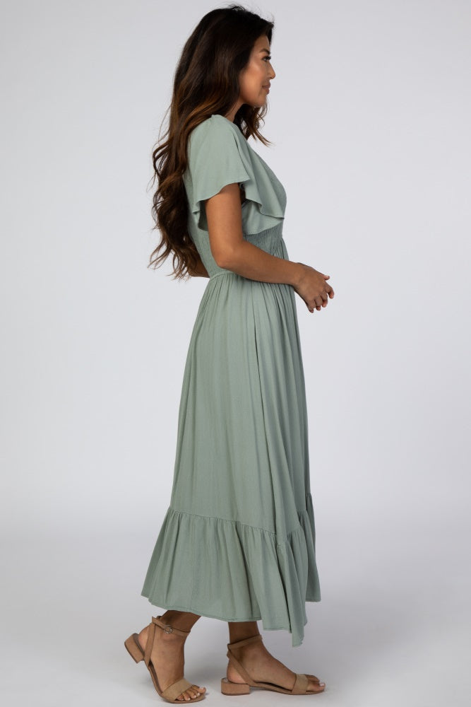 woman wearing a sage green maxi dress with short sleeves and a ruffled hem, standing sideways