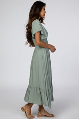 woman wearing a sage green maxi dress with short sleeves and a ruffled hem, standing sideways
