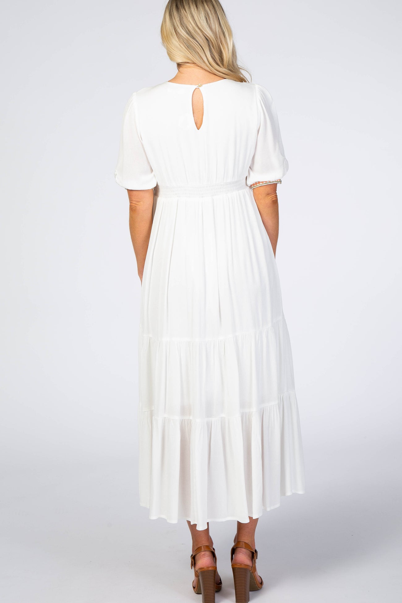 woman wearing a white maternity maxi dress with short puff sleeves and a tiered skirt, showing a keyhole back detail