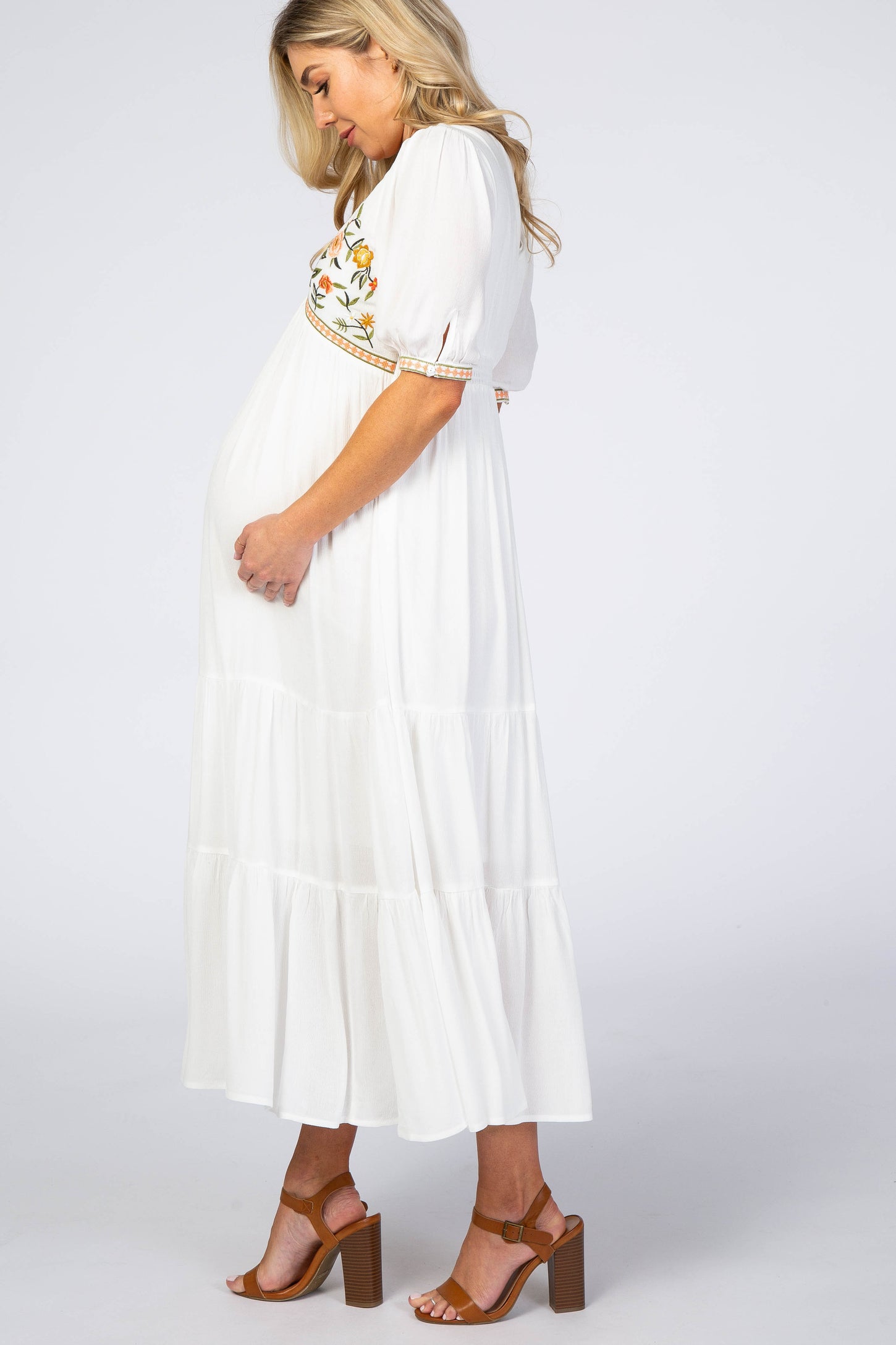 woman wearing a white maternity maxi dress with floral embroidery and a visible baby bump