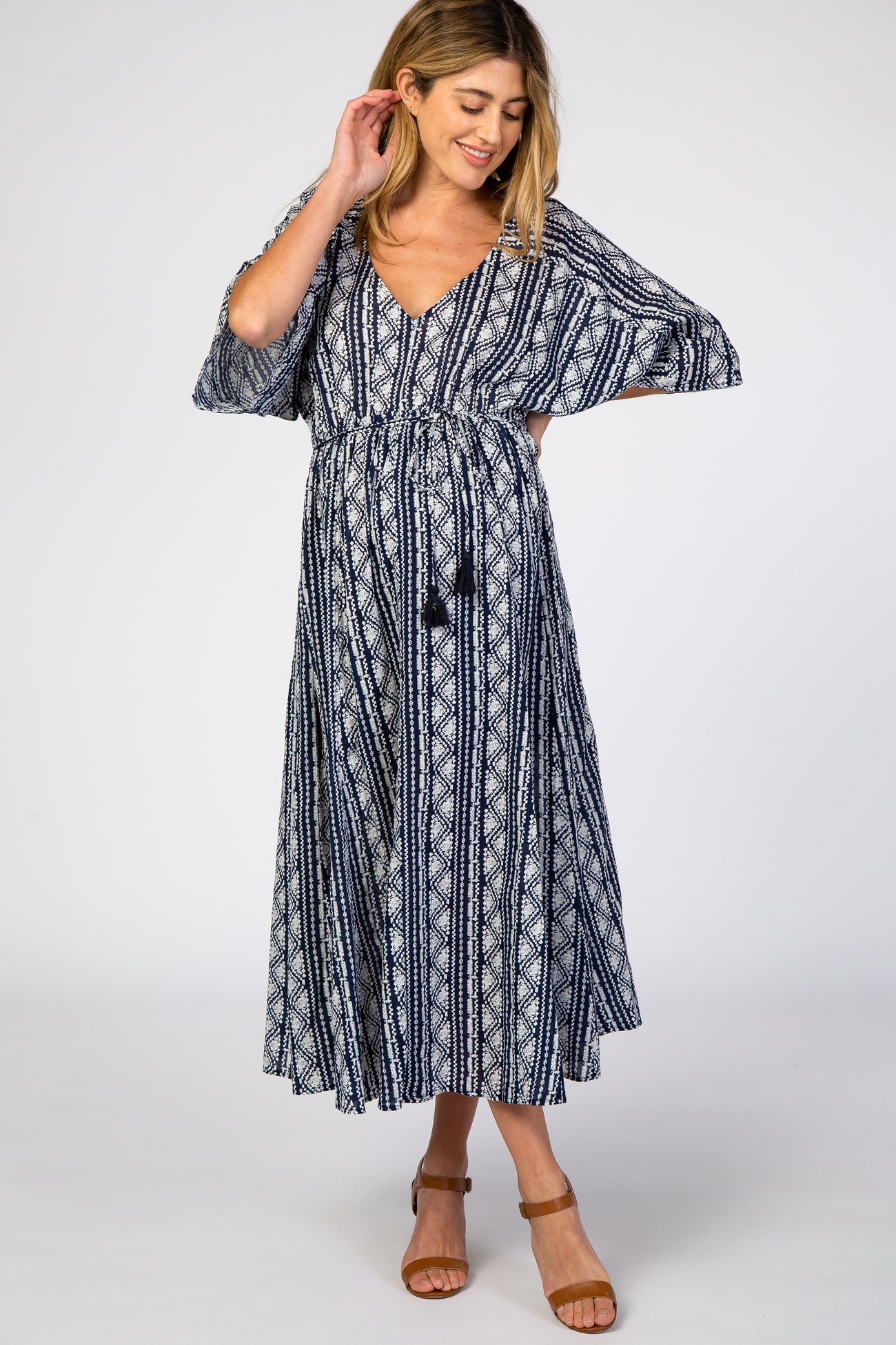 woman wearing a navy blue patterned maternity maxi dress with a v-neckline and tie waist, showcasing her baby bump