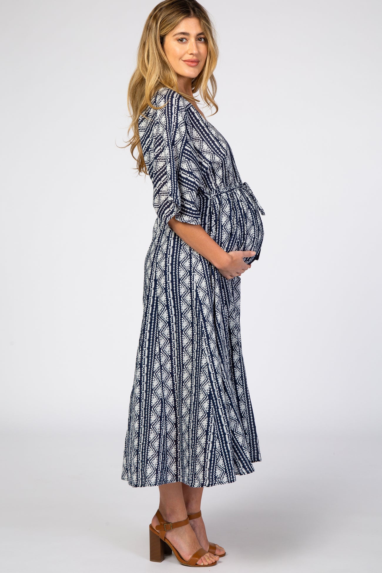 woman wearing a navy and white patterned maternity dress with a tie waist and holding her baby bump
