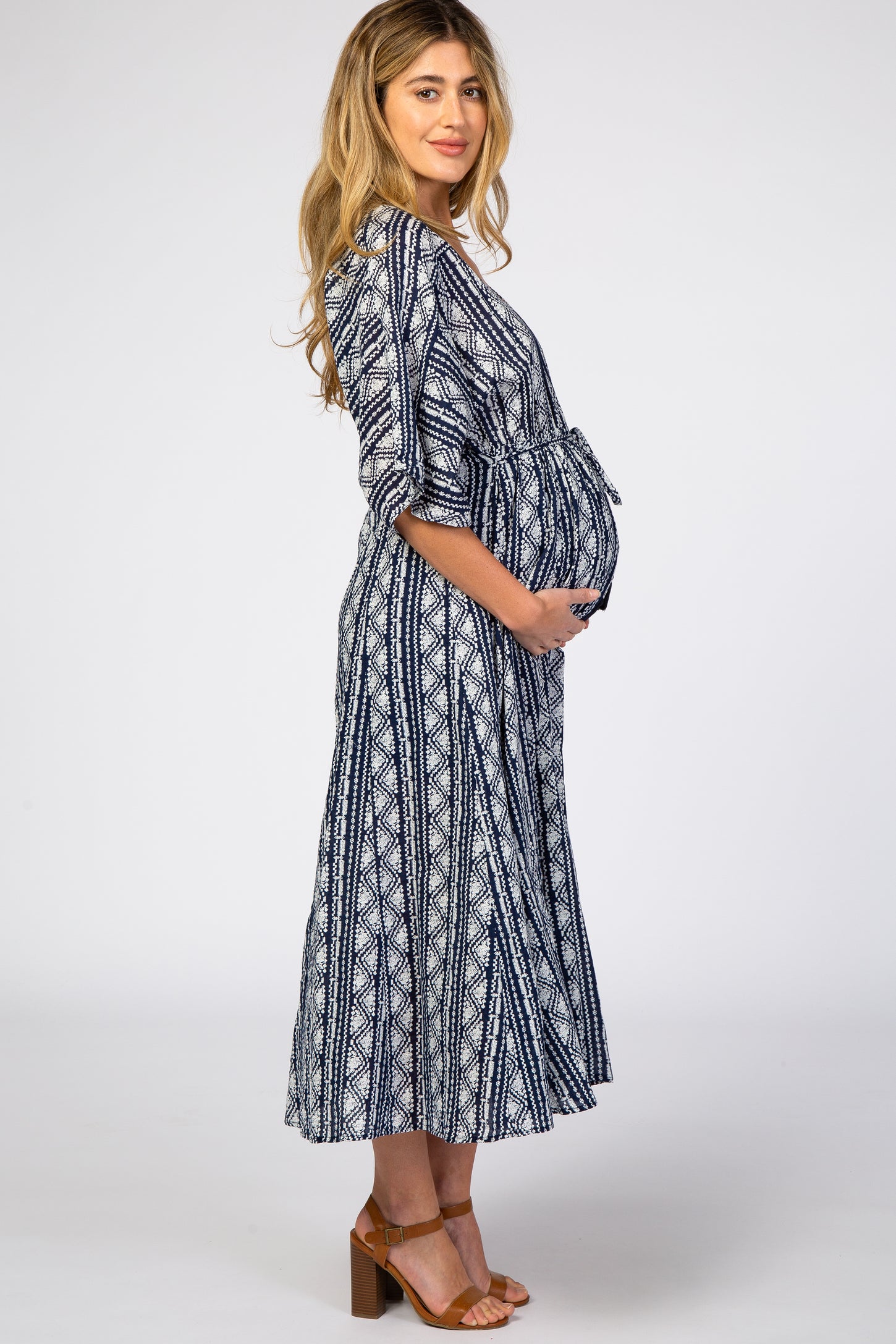 woman wearing a navy and white patterned maternity dress with a tie waist and holding her baby bump