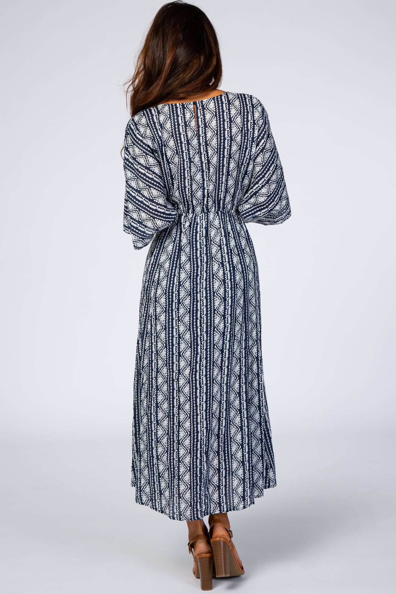 woman wearing a navy and white patterned maxi dress with a cinched waist and flowing sleeves, shown from the back