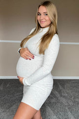 woman wearing a light gray long sleeve maternity dress and holding her baby bump