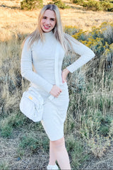 woman wearing a light gray long sleeve fitted dress with a drawstring side and a crossbody bag, standing outdoors