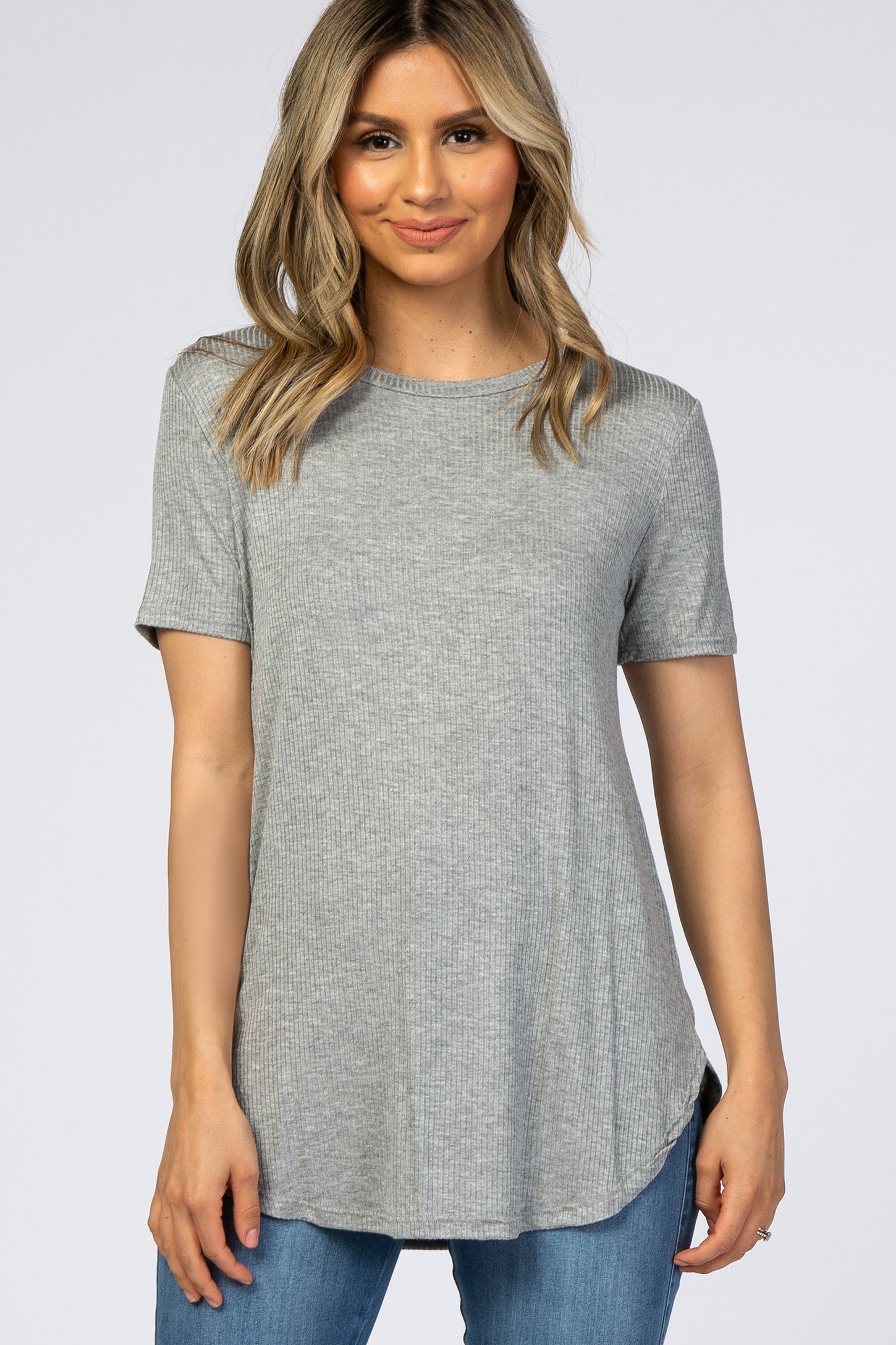 woman wearing a gray short sleeve ribbed top with a slight hem and side slits, paired with blue jeans