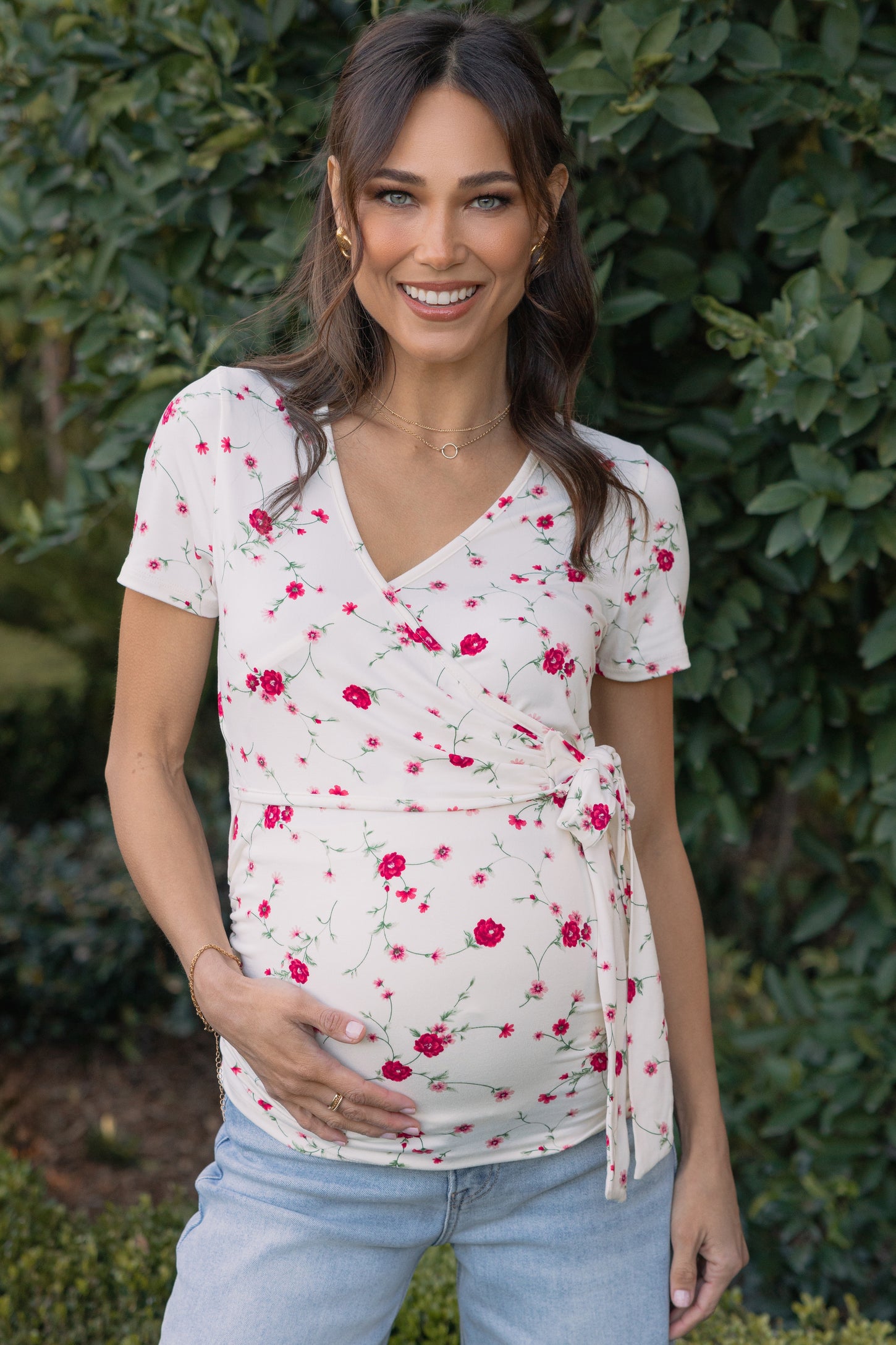 woman wearing a cream floral maternity wrap top and holding her baby bump