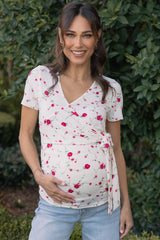 woman wearing a cream floral maternity wrap top and holding her baby bump