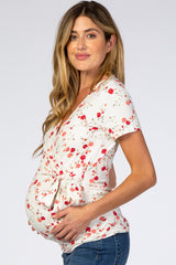 woman wearing a white floral print maternity top and holding her baby bump