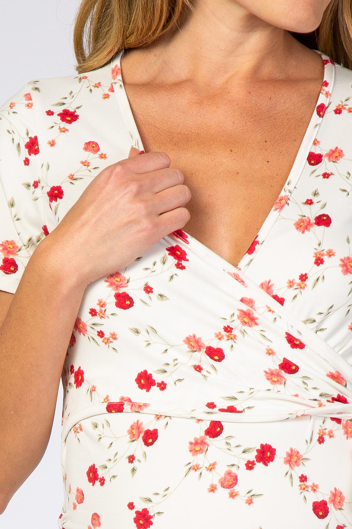 woman wearing a white floral maternity wrap top with short sleeves and a deep v-neck, holding the fabric near her chest