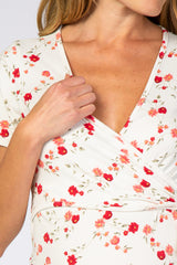 woman wearing a white floral maternity wrap top with short sleeves and a deep v-neck, holding the fabric near her chest