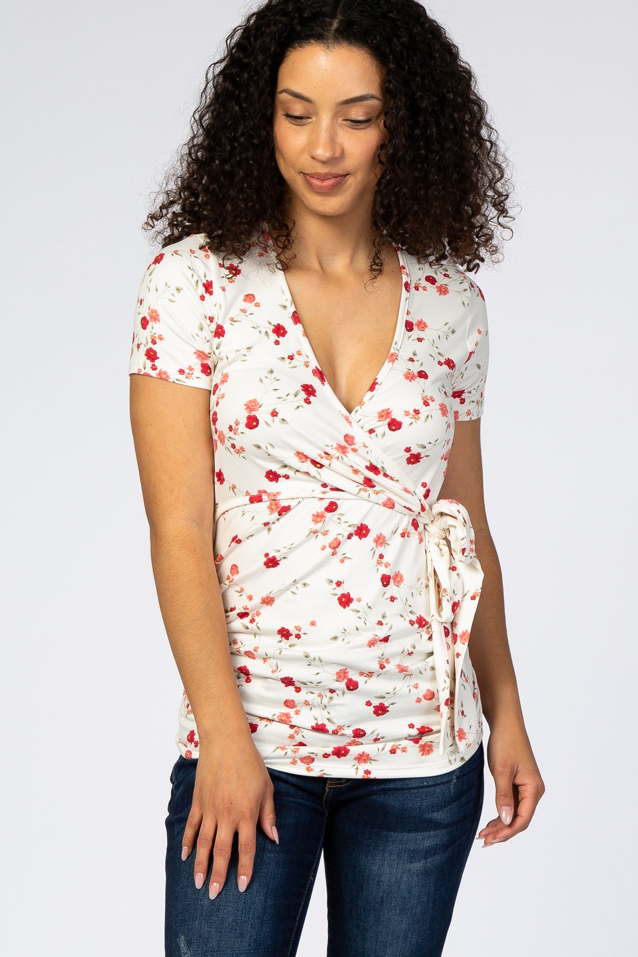 woman wearing a white floral short sleeve wrap maternity top with red flowers and blue jeans