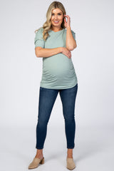 woman wearing a mint green short sleeve maternity top and dark blue skinny jeans, showing her baby bump