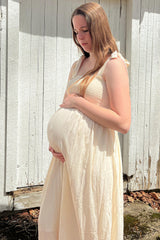 woman wearing a cream maternity dress with a fitted bodice and flowing skirt, holding her baby bump