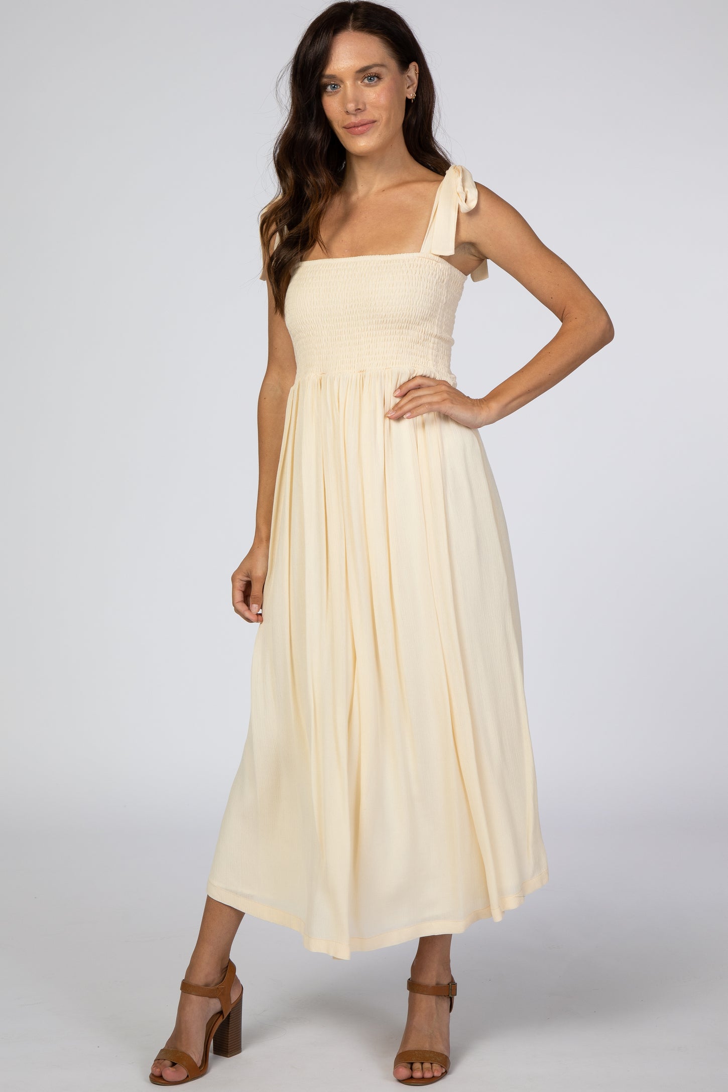 woman wearing a cream smocked maxi dress with a one-shoulder tie detail and a flowy skirt