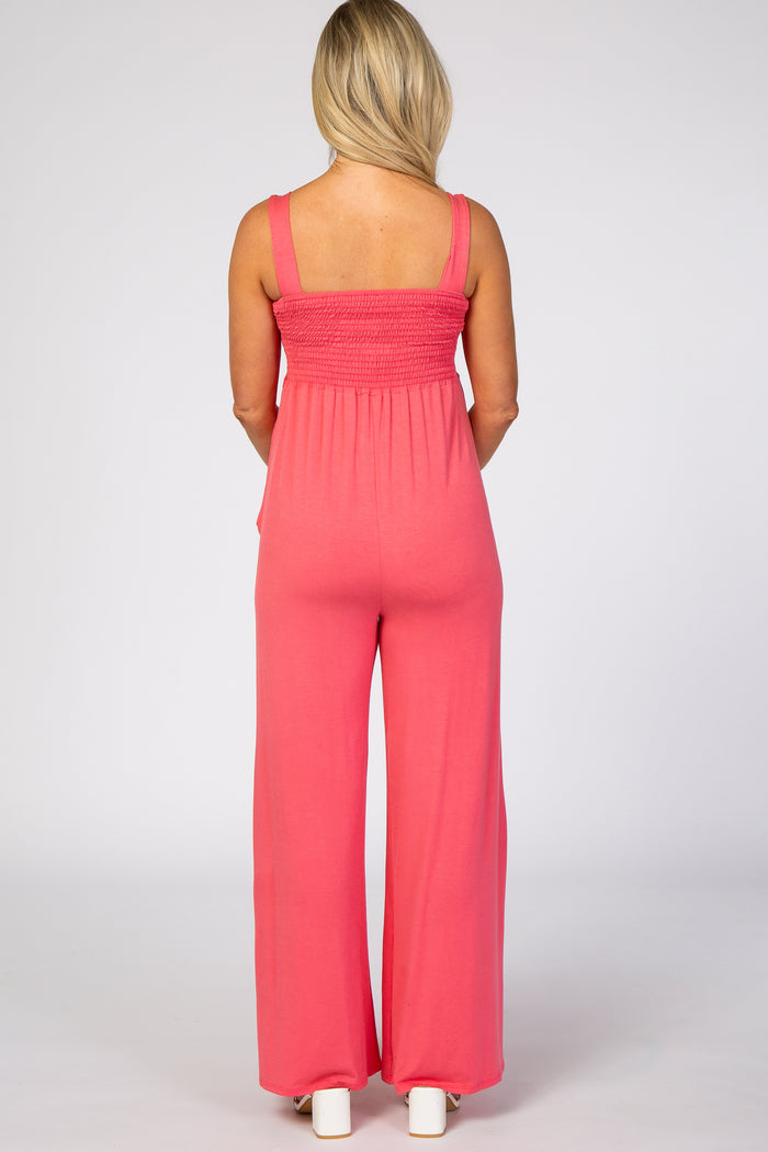 woman wearing a coral long dressy maternity jumpsuit with wide legs and smocked back detail