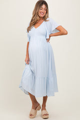 woman wearing a light blue maternity dress with short flutter sleeves and a tiered skirt, showcasing her baby bump
