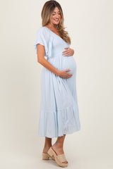 Pregnant woman in light blue smocked maternity midi dress holding her baby bump