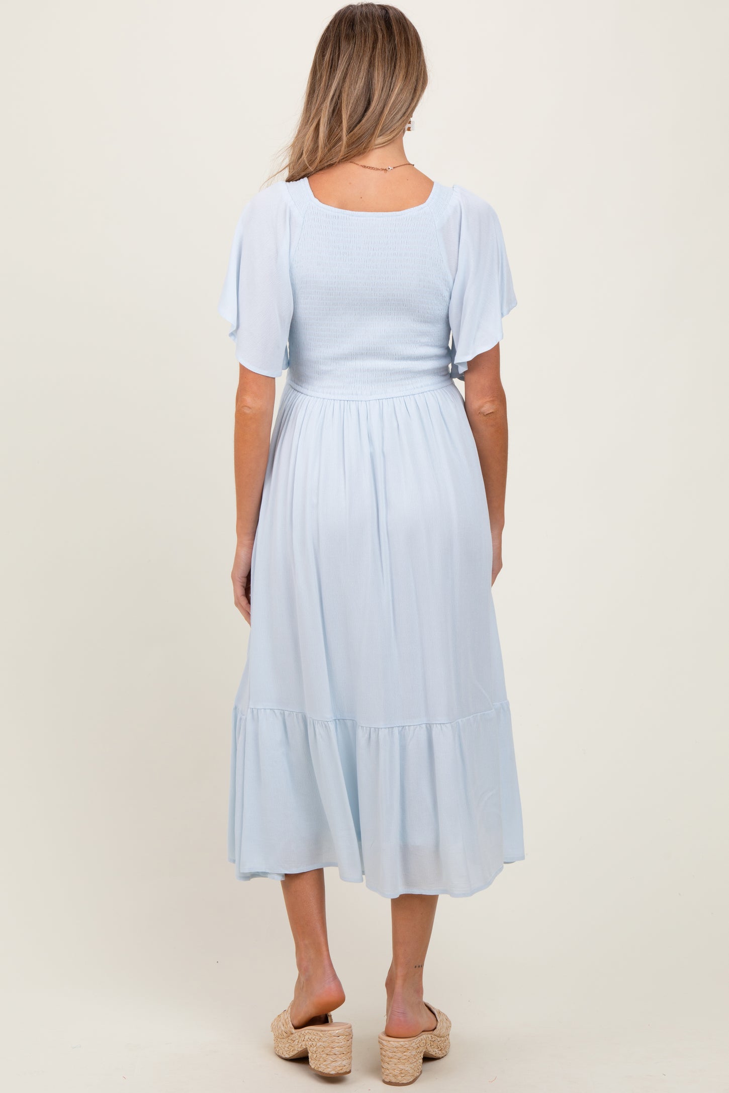 woman wearing a light blue maternity dress with a smocked bodice and tiered skirt, showing the back view