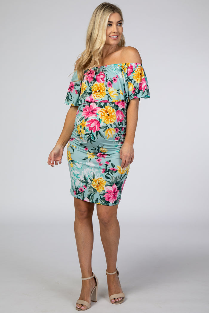 woman wearing a light blue off-the-shoulder floral maternity dress with a fitted silhouette and a visible baby bump