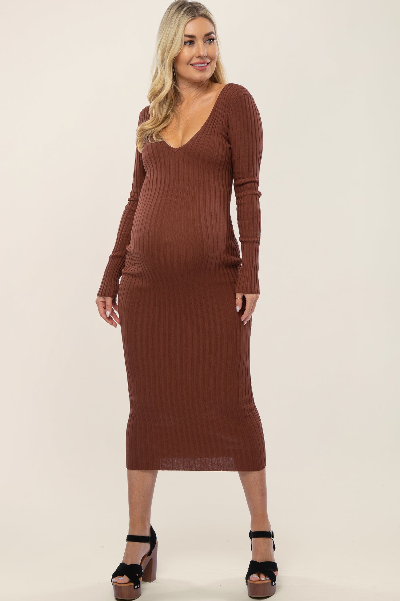 woman wearing a brown ribbed maternity dress with a deep v-neck and long sleeves, showcasing her baby bump