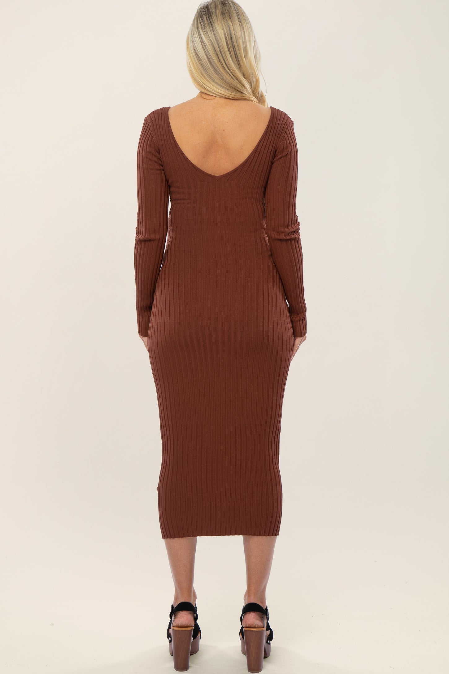 woman wearing a rust brown ribbed long sleeve maternity dress with a deep v-back, showing off her baby bump