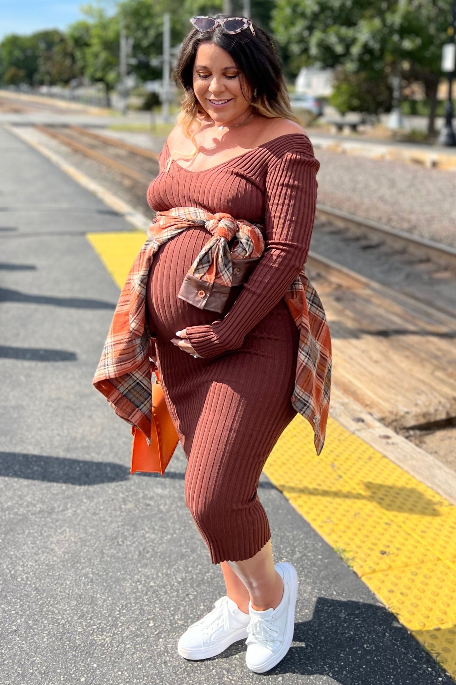 woman wearing a rust ribbed maternity dress with a plaid tied jacket and a visible baby bump