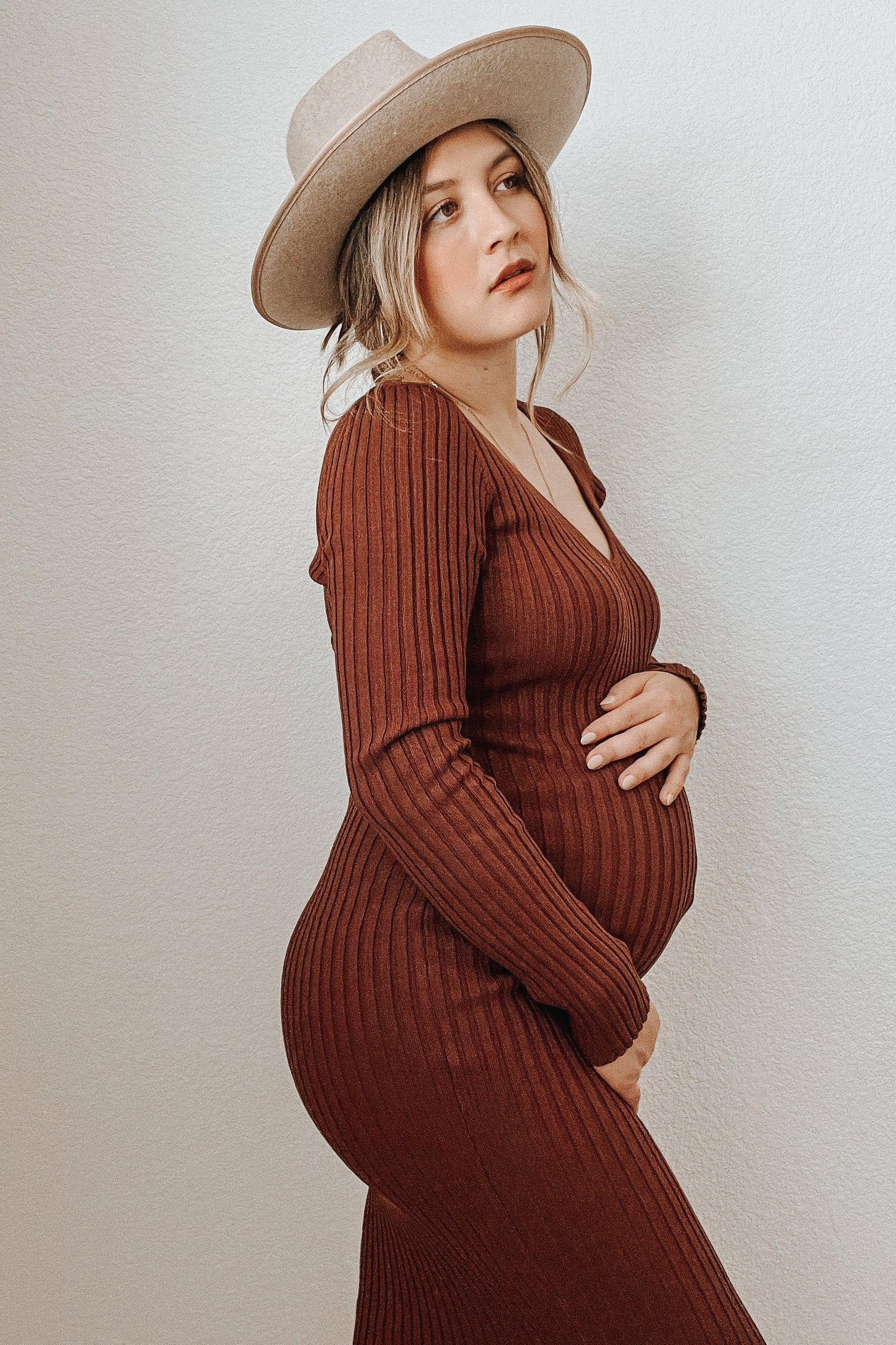 woman wearing a rust ribbed maternity dress and a wide-brimmed hat, highlighting her baby bump