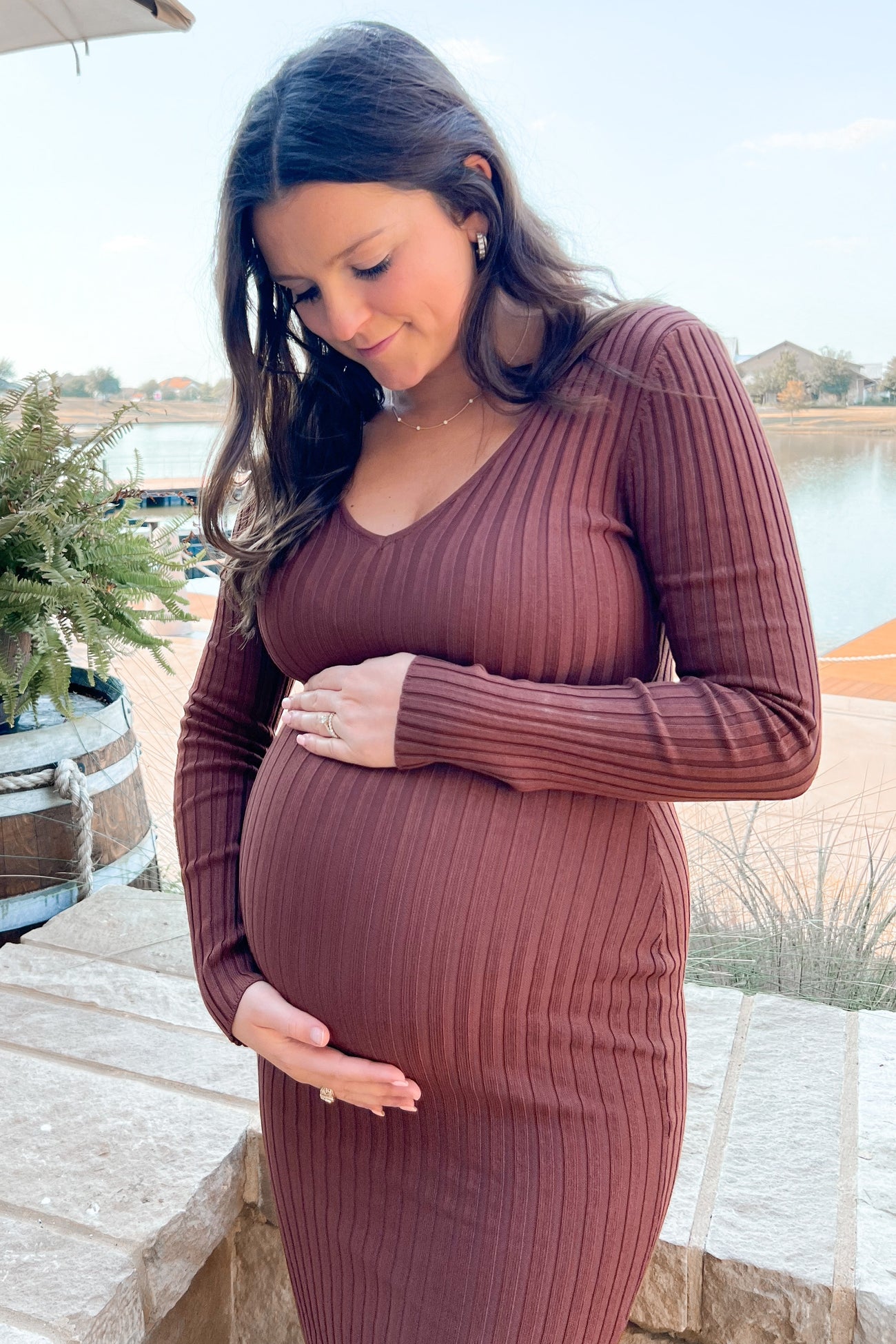woman wearing a brown ribbed long sleeve maternity dress, gently cradling her baby bump