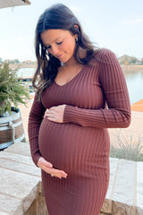 woman wearing a brown ribbed long sleeve maternity dress, gently cradling her baby bump