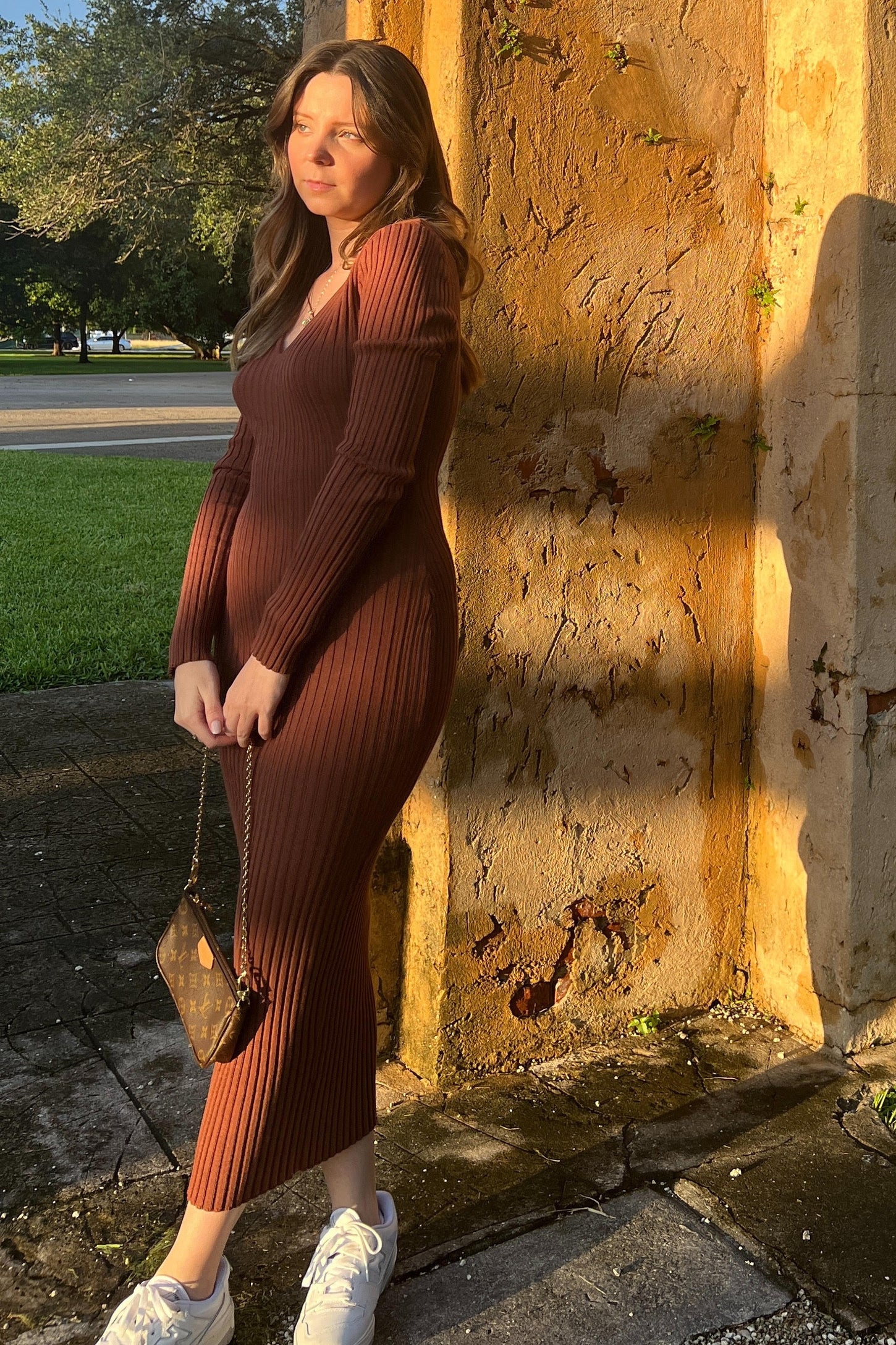 woman wearing a brown ribbed maternity dress that highlights her baby bump, paired with white sneakers and a small handbag