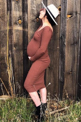 woman wearing a rust brown ribbed maternity dress, posing with a visible baby bump against a wooden background