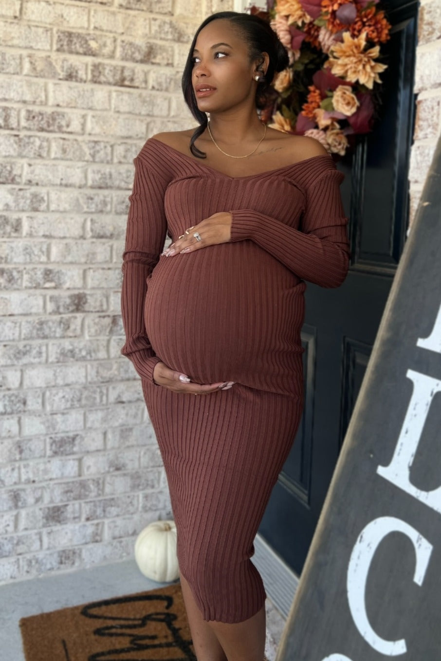 woman wearing a rust-colored off-the-shoulder maternity dress, showcasing her baby bump