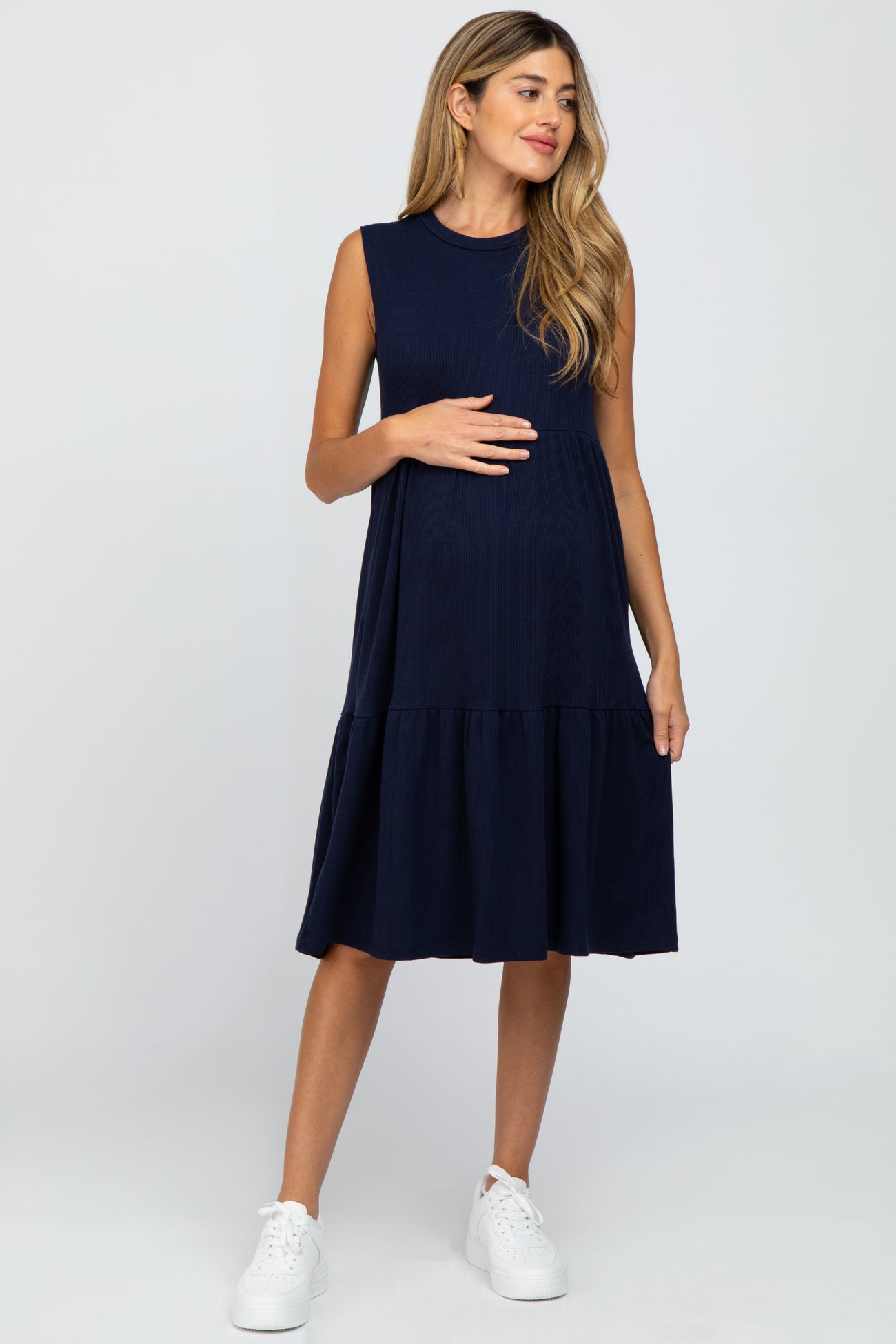 woman wearing a navy blue sleeveless maternity dress with a tiered skirt and holding her baby bump