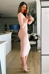 woman wearing a pink ribbed midi dress and holding a rose, standing in a well-decorated living space