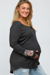 woman wearing a dark gray maternity top with patterned long sleeves and holding her baby bump