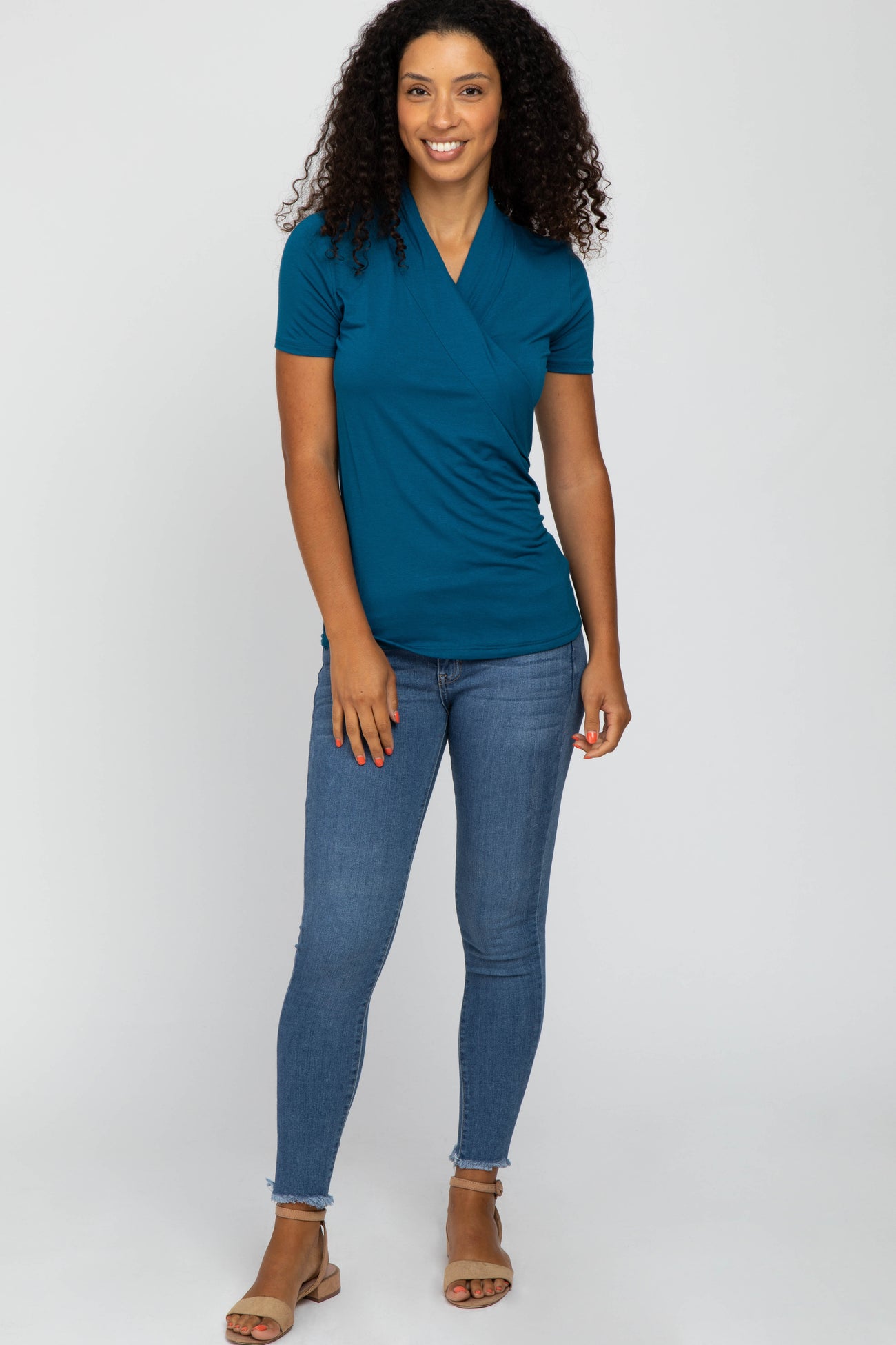 woman wearing a teal short sleeve wrap top with a v-neckline and paired with skinny jeans and sandals.