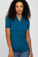 woman wearing a teal short sleeve wrap style top with draped detail and slim fit, paired with denim jeans