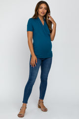 woman wearing a teal short sleeve crossover maternity top and showing her baby bump with fitted jeans and heels