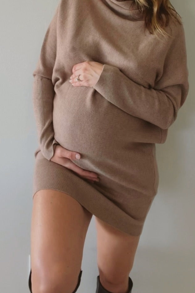 woman wearing a taupe long sleeve maternity sweater dress and holding her baby bump