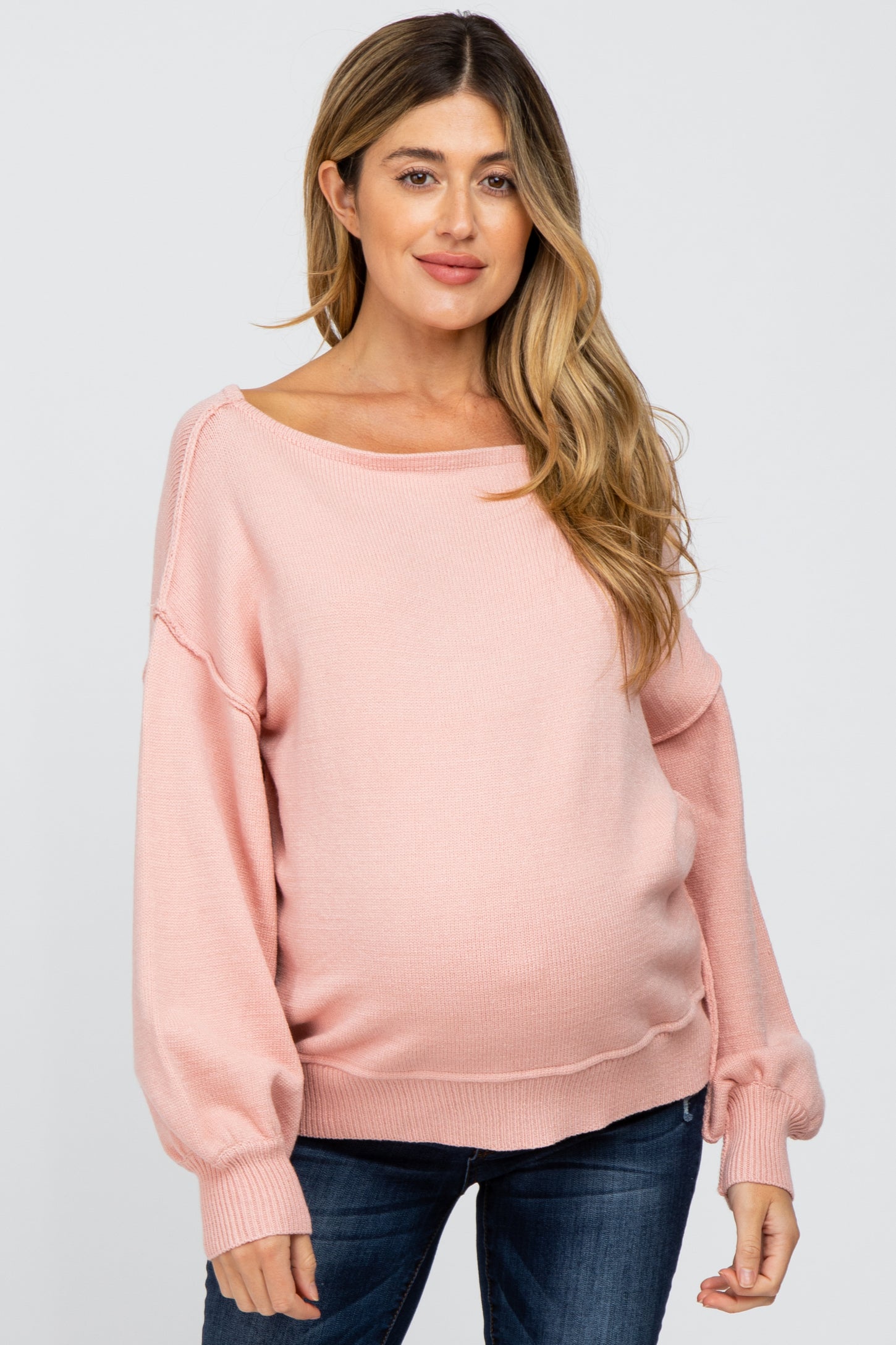 woman wearing a light pink maternity sweater with a loose fit and long sleeves, showcasing her baby bump