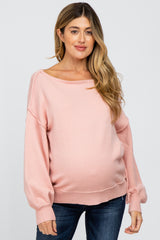 woman wearing a light pink maternity sweater with a loose fit and long sleeves, showcasing her baby bump