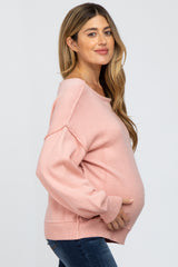woman wearing a soft pink oversized maternity sweater and holding her baby bump