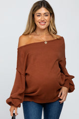woman wearing a rust off-the-shoulder maternity sweater with a visible baby bump, holding a black umbrella