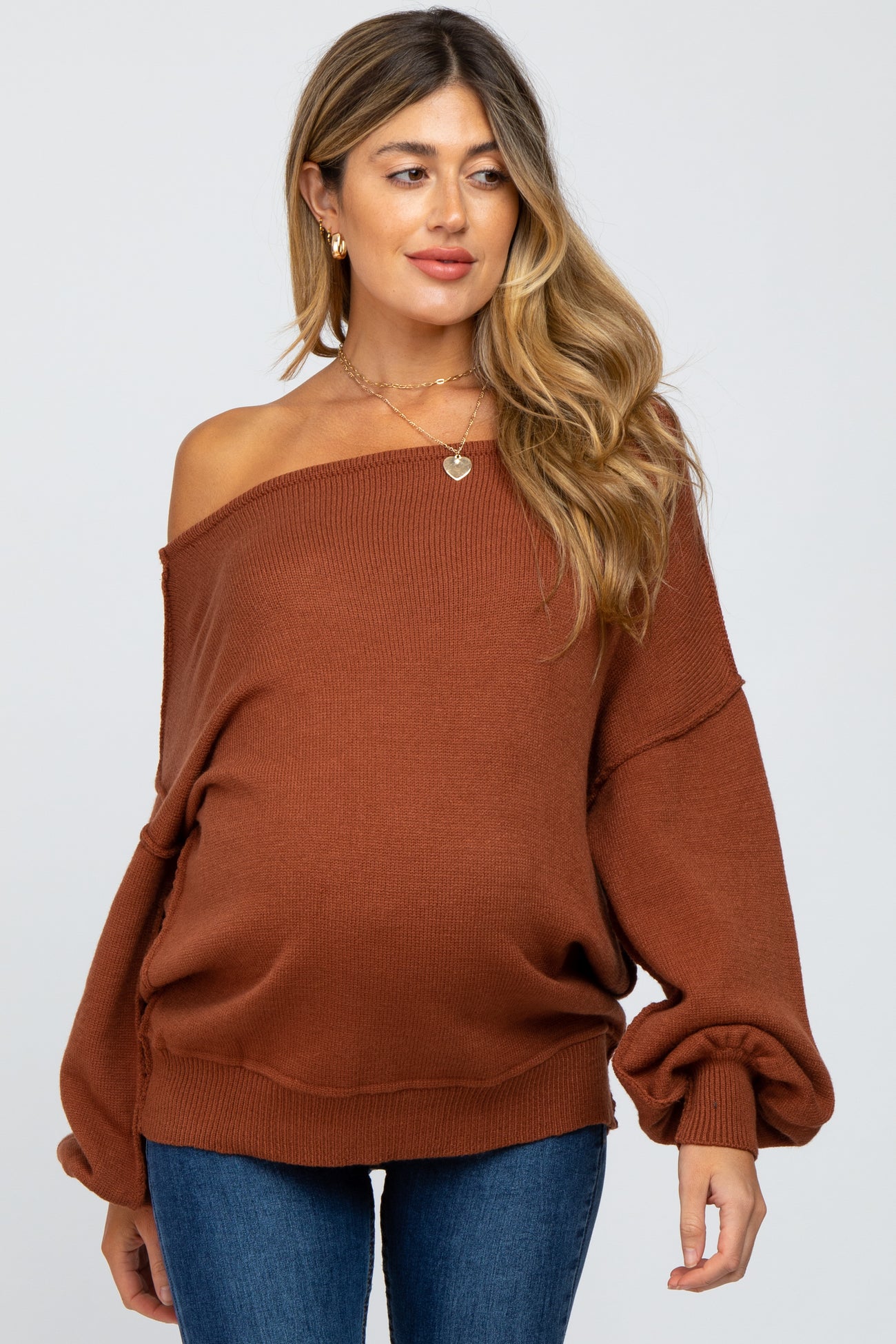 woman wearing a rust oversized off-shoulder maternity sweater and showing her baby bump